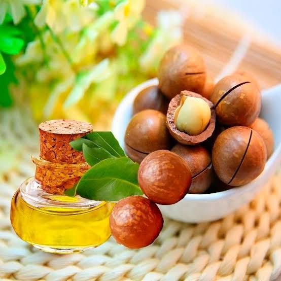 Noix de macadamia dans un bol et flacon d'huile ambrée sur un set en rotin